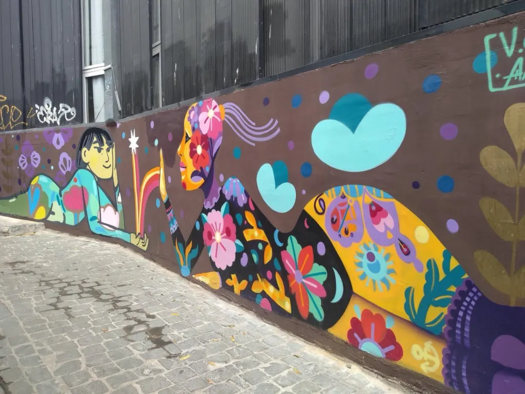 Mural colorido de dos figuras con flores junto a una calle empedrada de Valparaíso