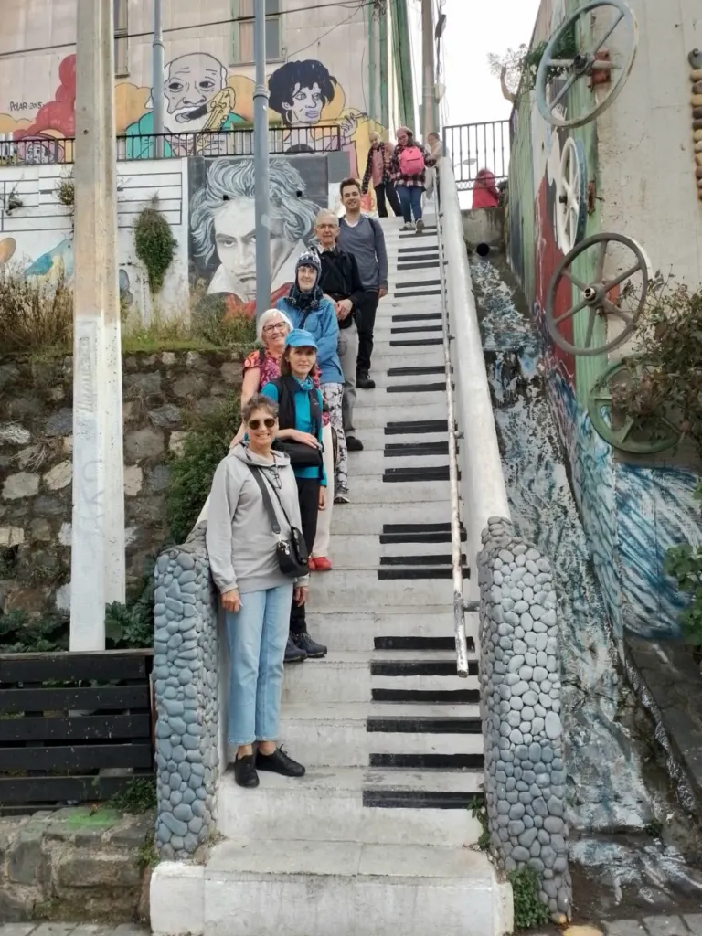 Grupo de visitantes en una escalera pintada como teclado de piano, con murales, en un cerro de Valparaíso