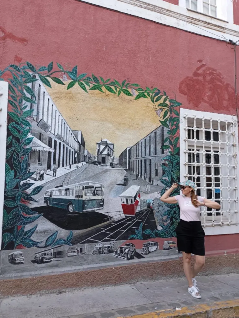 Visitante frente a un mural de una calle antigua de Valparaíso con un trolebús y un carro de ascensor