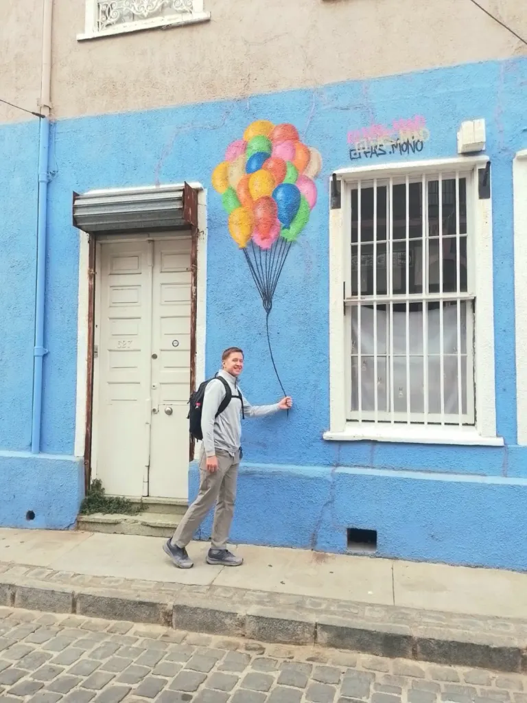 Visitante junto al mural de los globos de colores en una casa azul de Valparaíso