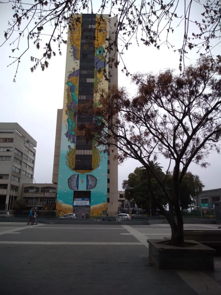 Edificio con un gran mural urbano junto a una plaza arbolada