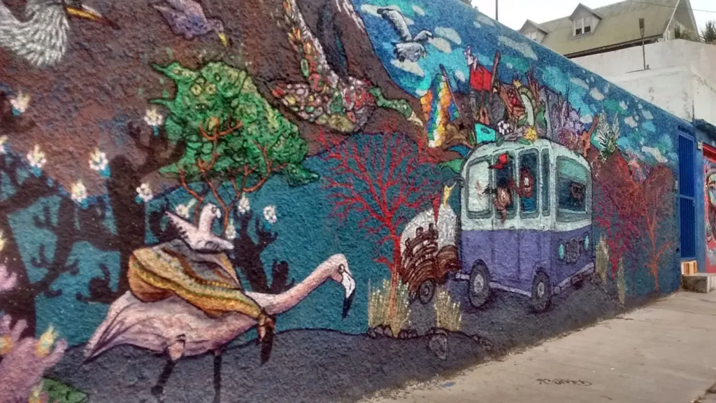 Mural con flamingos, un bus violeta y flora en un muro de Valparaíso